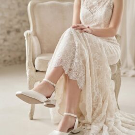 Seated bride wearing ivory satin Helen bridal shoes with low block heel and ankle straps